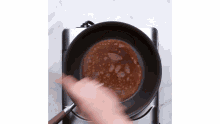 a person is stirring a pan of liquid on a stove .