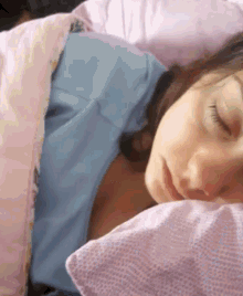 a woman in a blue shirt is sleeping in a bed with a pink pillow