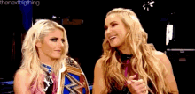 two female wrestlers are standing next to each other in a ring and smiling .