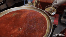 a person pouring liquid into a pan of tomato sauce with the words made in animotica visible