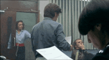 a man in a blue shirt is holding a piece of paper in front of a woman