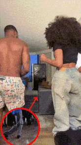 a shirtless man and a woman are dancing in a living room with a red arrow pointing to the woman 's butt