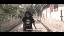 a woman wearing a black shirt with a skull and crossbones on it is walking down a street .