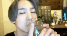 a woman drinking from a glass in front of a sign that says " shots "