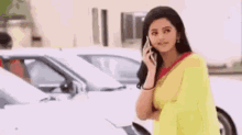 a woman in a yellow saree is talking on a cell phone in front of a car .