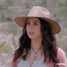 a woman wearing a straw hat and a pink cardigan is standing in a field .