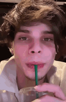 a young man with a piercing in his lip drinks through a straw