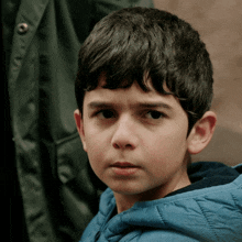 a young boy wearing a blue jacket with a hood looks at the camera
