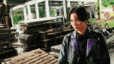 a man in a black and purple leather jacket stands in front of a pile of wooden pallets