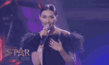 a woman is singing into a microphone while wearing a black feathered coat .