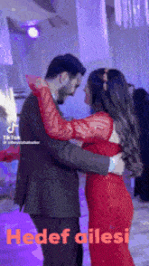 a man in a suit and a woman in a red dress are dancing together with the words hedef ailesi behind them
