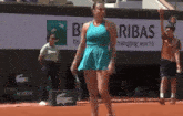 a woman in a blue dress is walking on a tennis court in front of a bnp paribas banner