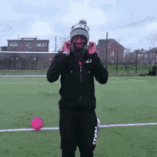 a man wearing a beanie is standing on a soccer field with a pink ball