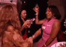 a group of women are toasting with wine glasses while standing around a table .