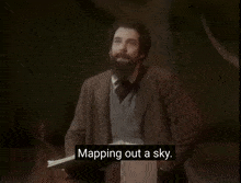 a man with a beard stands in front of a piano and says what you feel like planning a sky