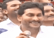 a man with a mustache is smiling and holding a microphone in front of a crowd .