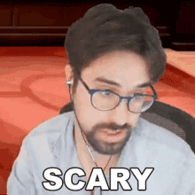 a man with glasses and a beard is making a scary face while sitting at a table .