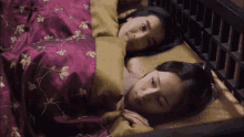 two women laying under a purple blanket with gold embroidery