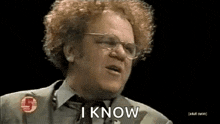 a man with curly hair and glasses is wearing a suit and tie and says `` i know '' .