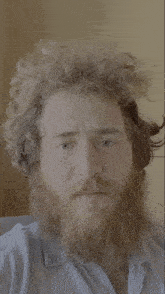 a man with a beard wipes his eye with his hand