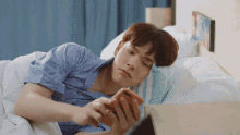 a young man laying in bed looking at his cell phone