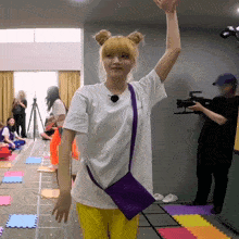 a woman in a white t-shirt and yellow pants holds her arm up