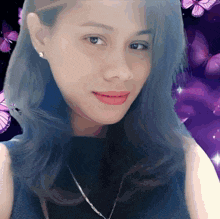 a woman with blue hair and purple butterflies in the background looks at the camera