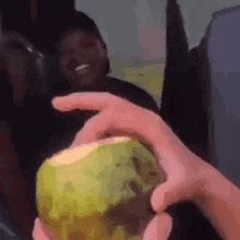 a person is holding a coconut in their hand in front of a man .