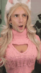 a man is wearing a pink sweater with a heart cut out in the chest and a cat ear headband .