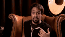 a man with a beard is sitting in a chair with his hands in his pockets