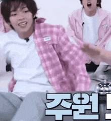 a man in a pink plaid shirt is sitting on a bed next to a man in a pink jacket .