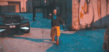 a man in a black jacket and yellow shorts is standing in front of a black car in a video game .