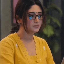 a woman wearing glasses and a yellow shirt is sitting in front of a laptop computer .