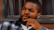 ice cube is sitting in front of a window with his hand on his chin and a serious look on his face .
