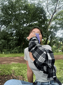 a girl in a plaid shirt is sitting in the grass