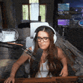 a woman wearing headphones and glasses is sitting at a desk in front of a microphone