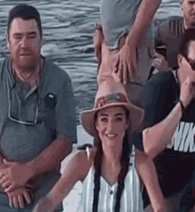 a group of people are sitting on a boat in the water . the woman is wearing a hat and smiling .
