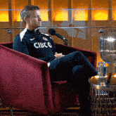 a man is sitting in a chair wearing a cibco shirt