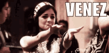 a woman is blowing a kiss in front of a group of people and the word venez is on the bottom .