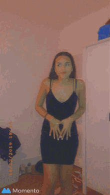 a woman in a black dress is standing in a room with a momento icon on the bottom right