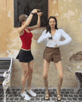 two women are dancing in front of a brick wall and a purple bench