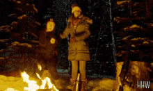two people standing in front of a fire with the letters hw on the bottom left