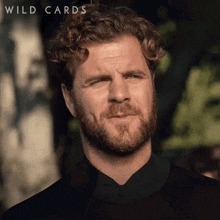 a man with a beard is wearing a wetsuit and the word wild cards is on the bottom of the image