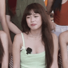 a woman wearing a green tank top and a necklace is sitting in a crowd of people .
