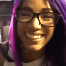 a close up of a woman wearing glasses and purple hair smiling