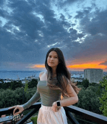 a woman is standing on a balcony at sunset wearing a smart watch .