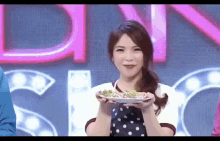 a woman is holding a plate of food in front of a sign that says ' dyn '