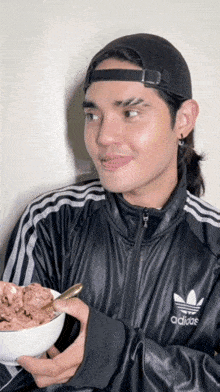 a man wearing an adidas jacket holds a bowl of ice cream