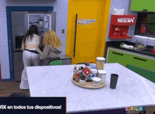 two women in a kitchen with a nescafe machine on the wall