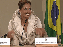 a woman in a fur coat is sitting at a table with a name plate that says francisbel dos santos